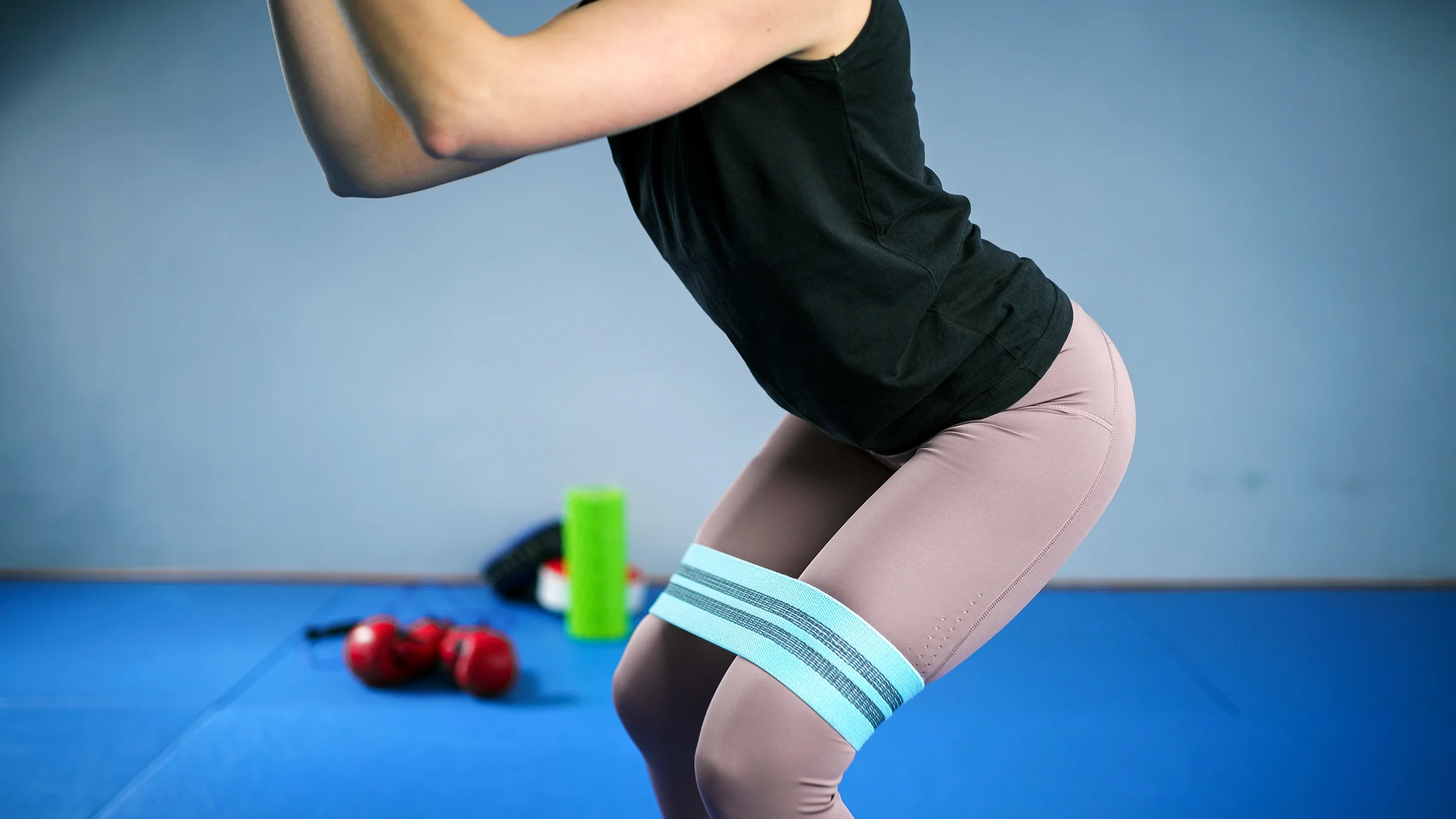 A woman wears a resistance band around her thighs while doing a squat.