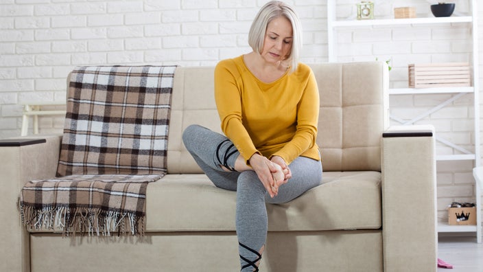 A person sitting on their couch, examining their foot.