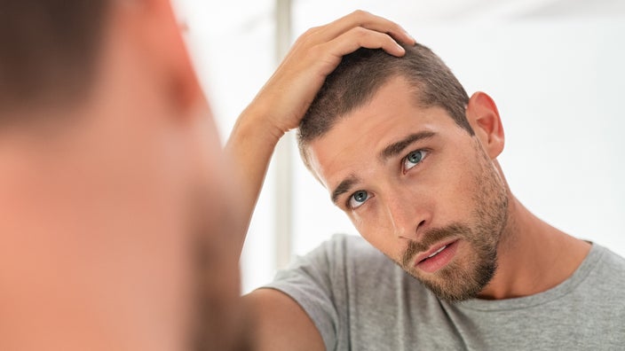 Man looking in the mirror at a dry, bald patch on his scalp.