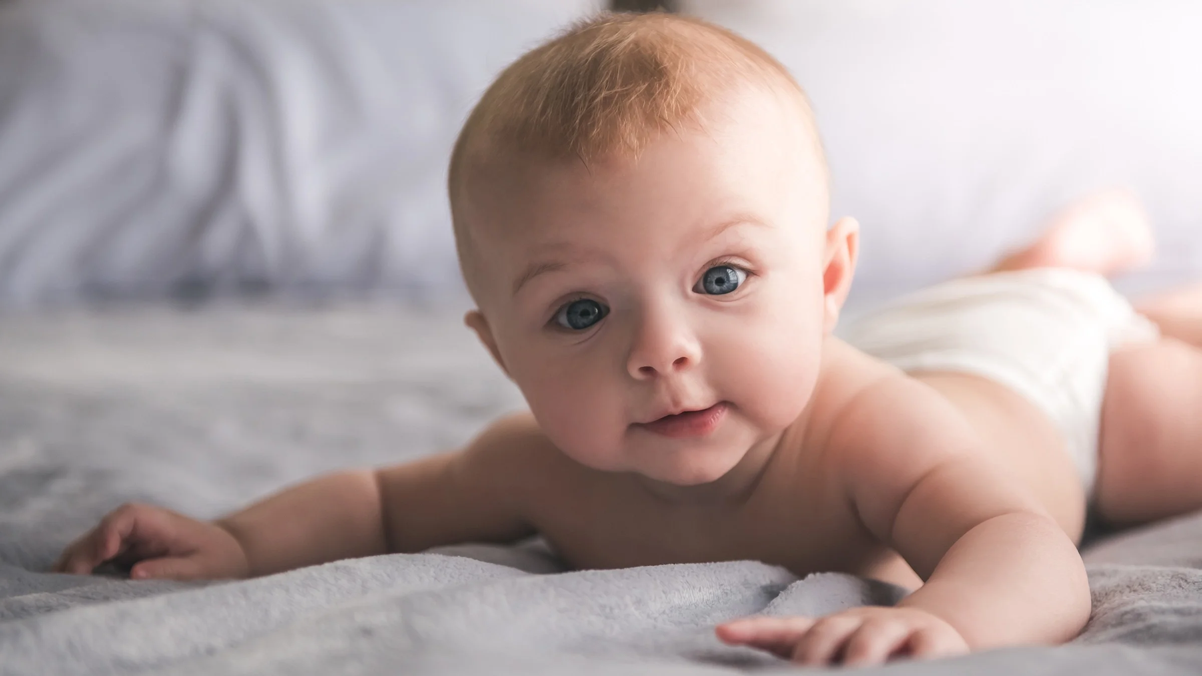 Portrait of a baby laying on its stomach holding its head up. Their head is slightly odd-shaped or seemingly larger than average.