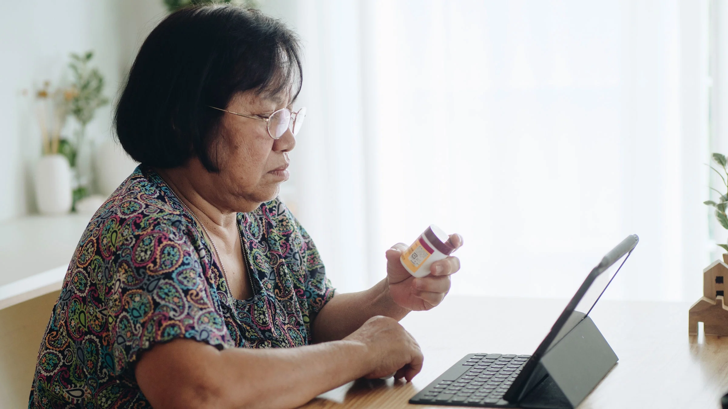 Senior woman with digital tablet checking prescription label in living room at home.
