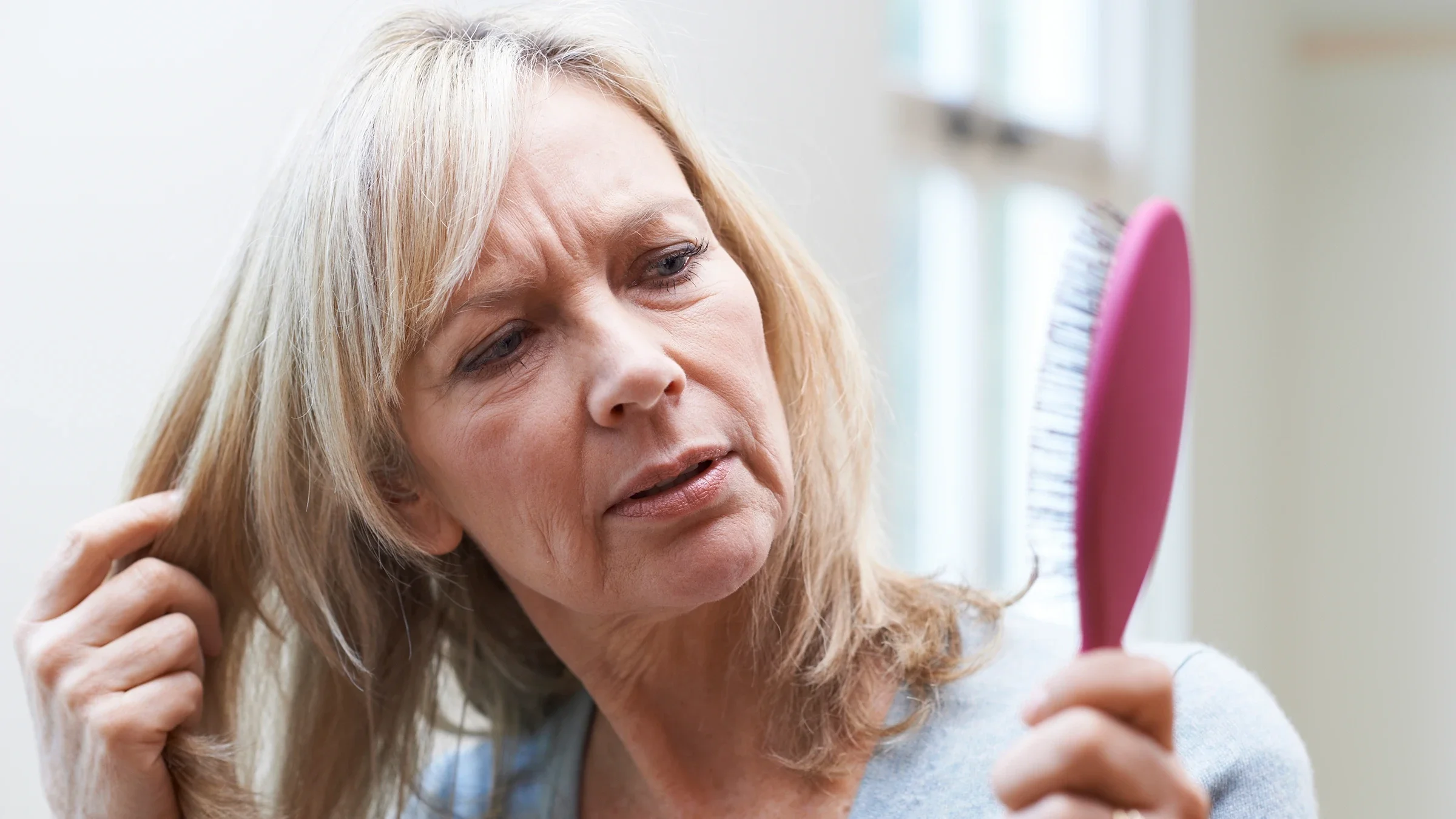 A woman examines her hairbrush with concern about hair loss.