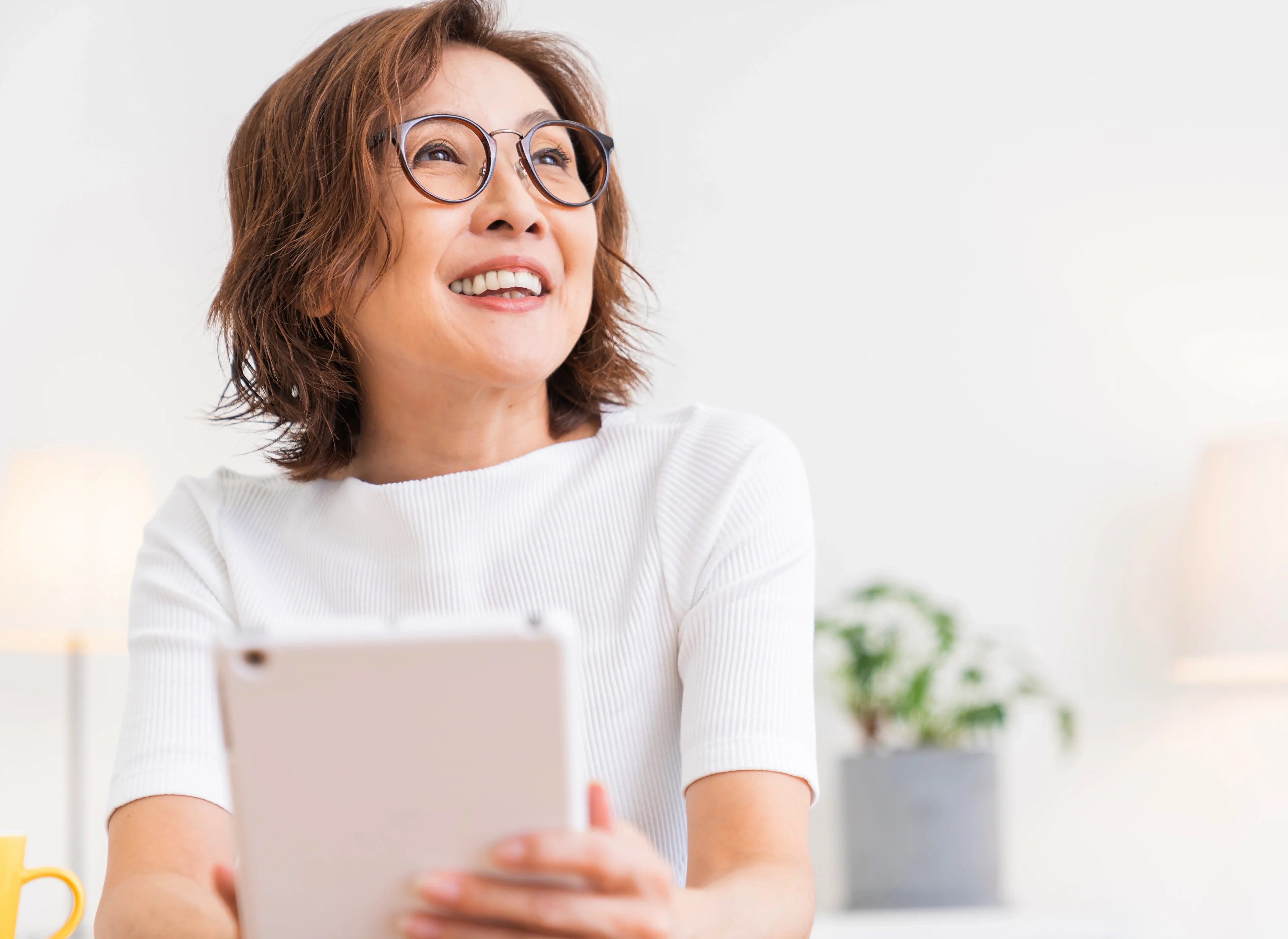 A smiling woman with glasses using an electronic tablet.