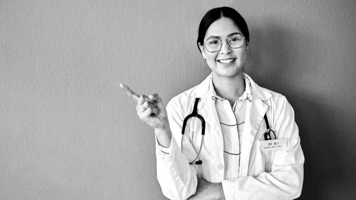 Portrait of a doctor in glasses wearing a lab coat and stethoscope with her finger pointing off to the side.
Moyo Studio/E+ via Getty Images