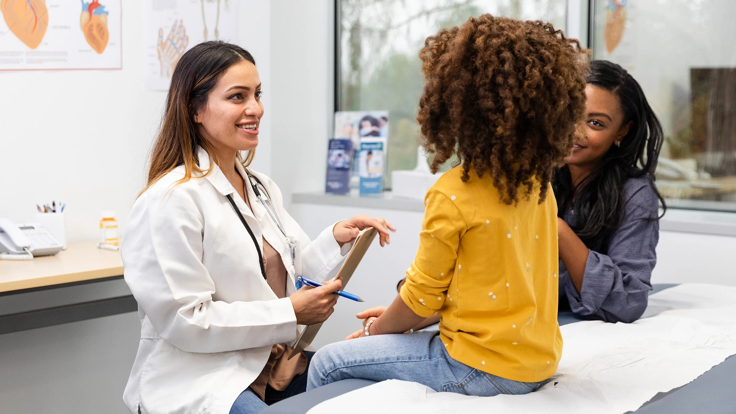 A healthcare professional talks with a girl and her mother during an appointment. 