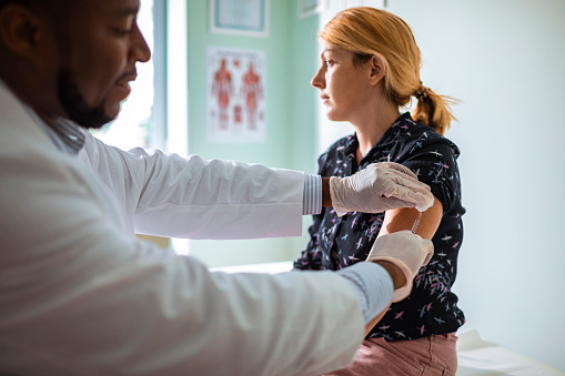 Close-up of a woman getting a shot at the doctors office looking away from her arm and the doctor.