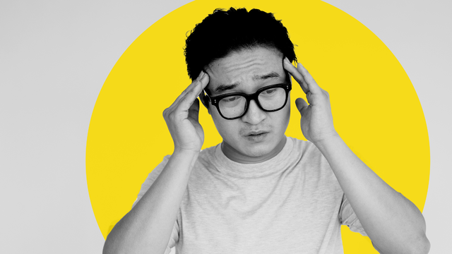 Black and white studio portrait of a man holding his hands to his temples. There is a graphic yellow circle added behind him.