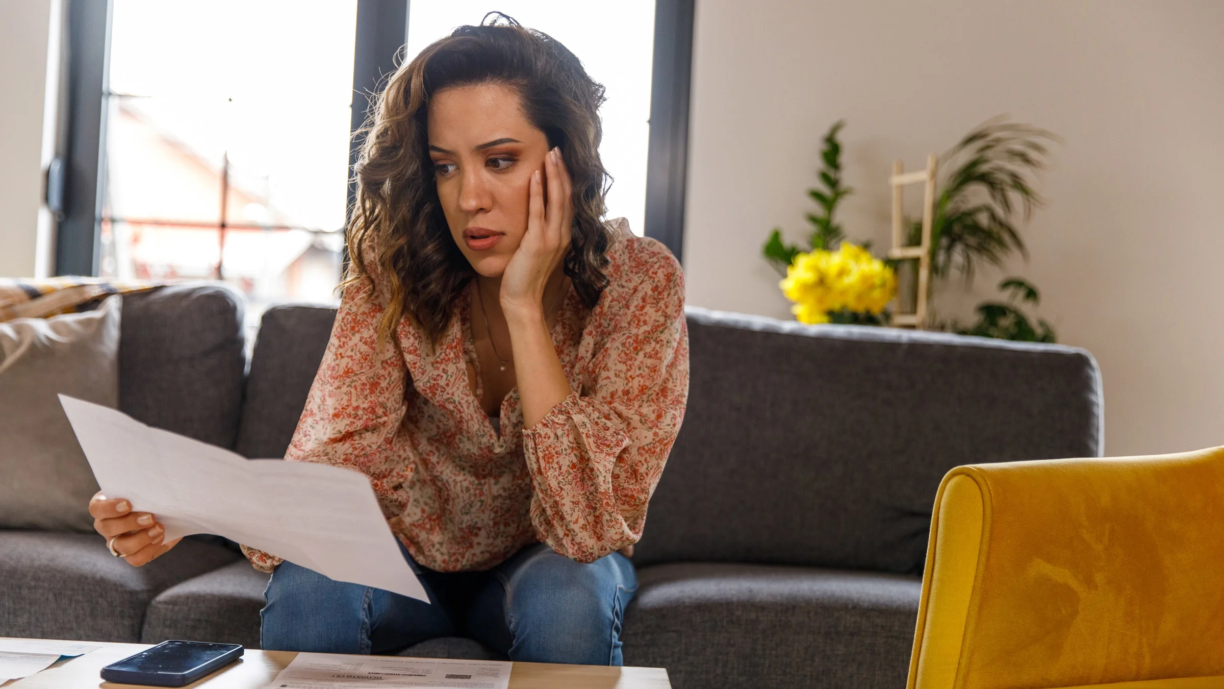 A person sitting at their couch, worried about their bills.