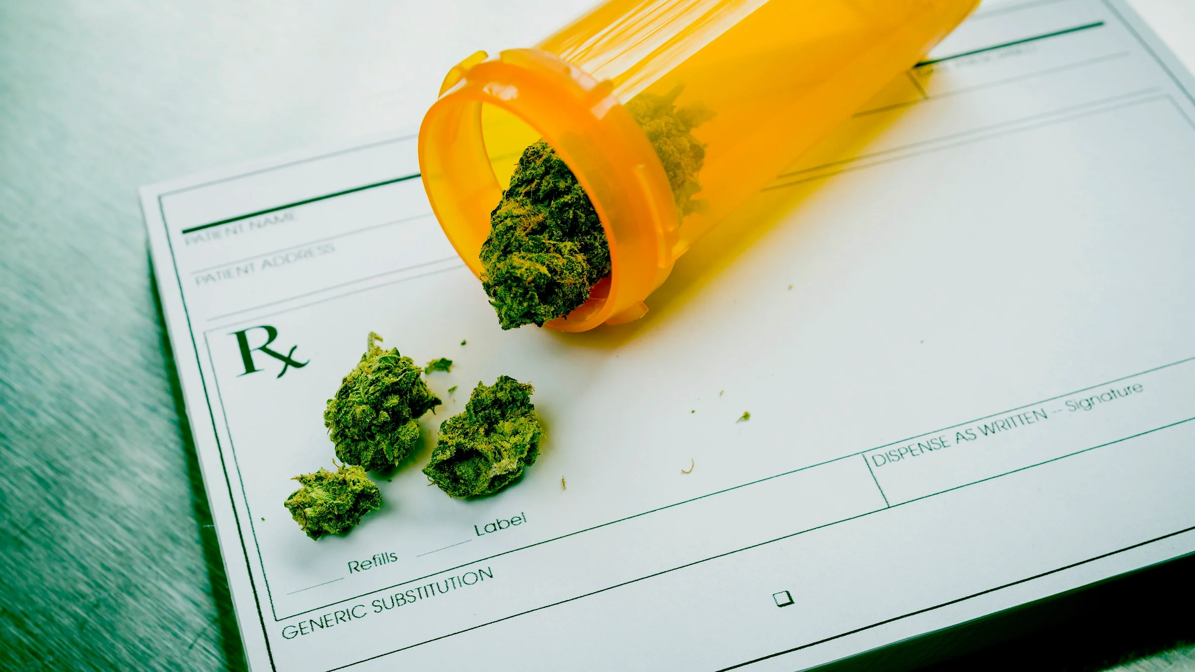 Prescription bottle filled with weed spilling out on a prescription pad.