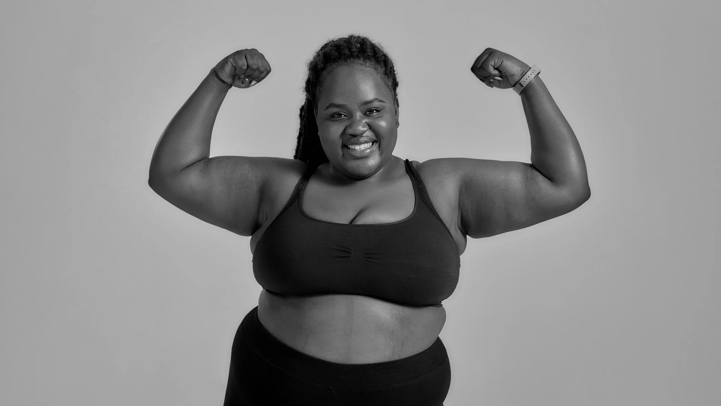 Black and white portrait of a plus size woman flexing booth arms and smiling.