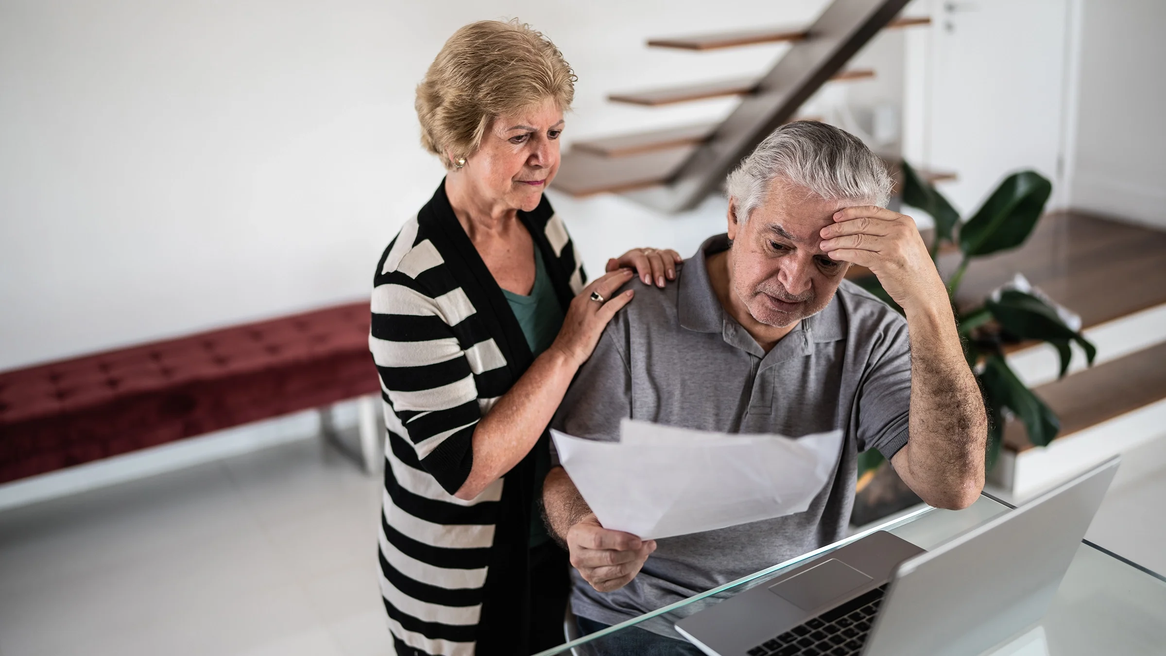 A senior couple look concerned while going through bills at home.
