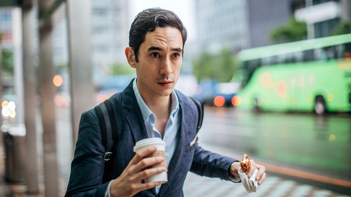 A man walks on the street with coffee and breakfast.