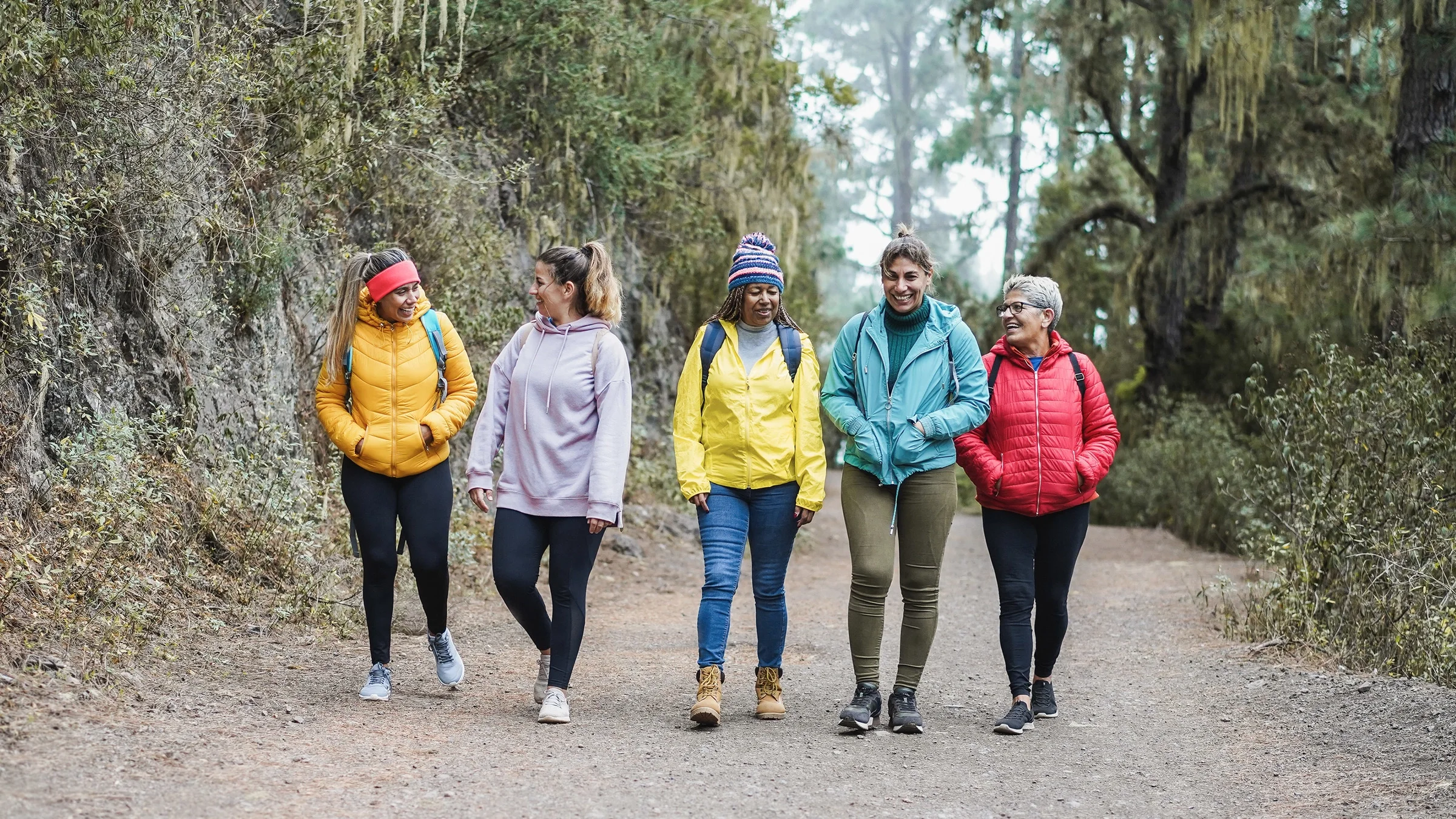 A group of multiracial middle-aged friends hiking in colorful clothes.