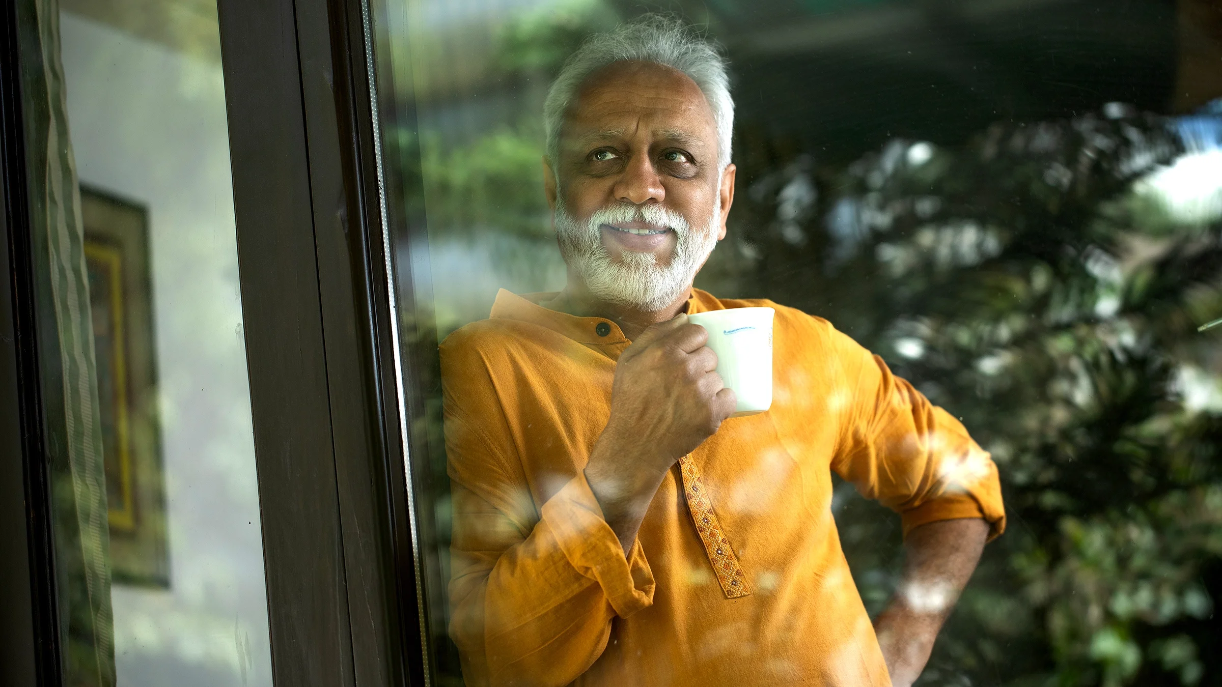 A man drinks a cup of coffee while looking out the window. 