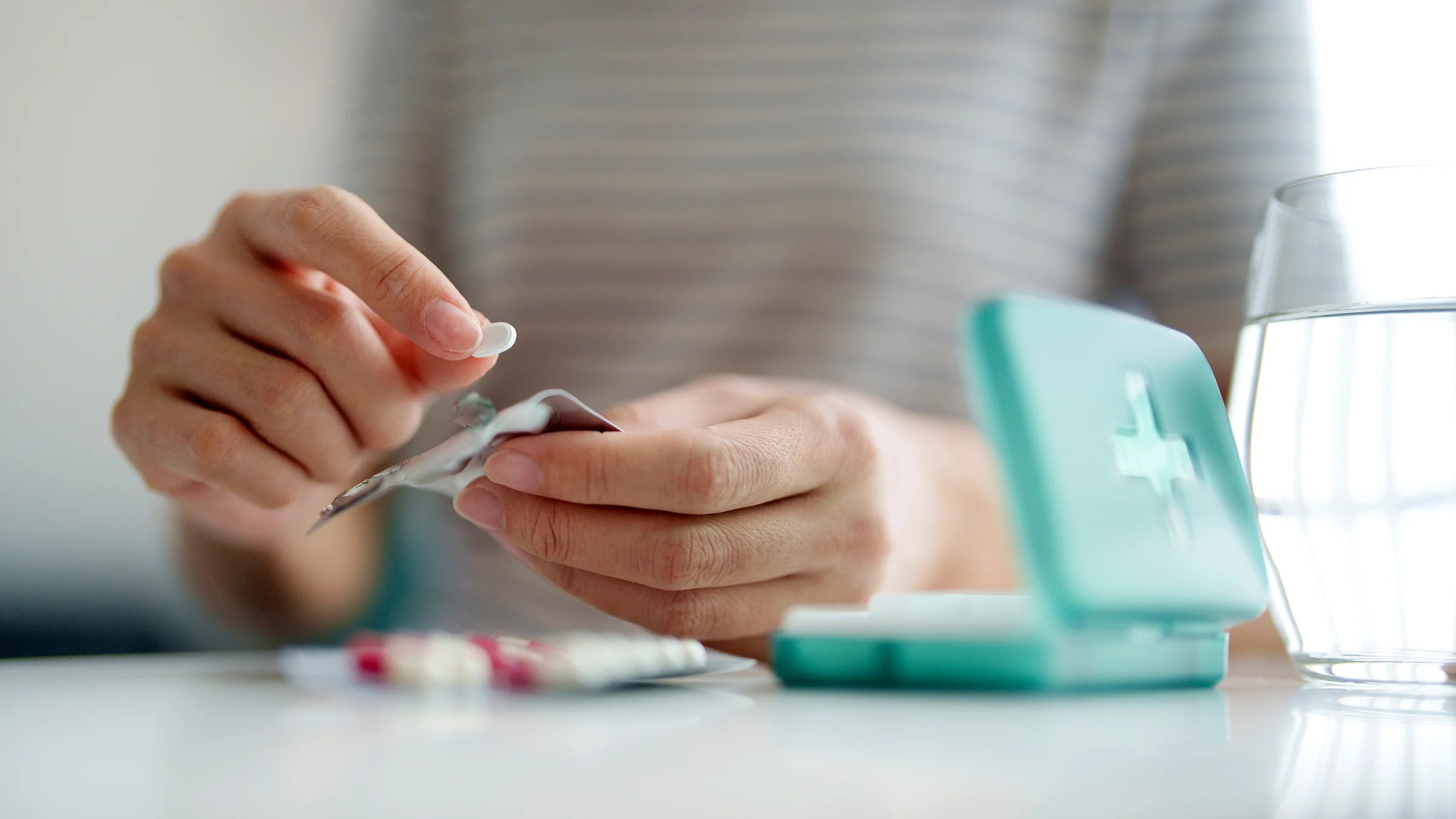 A woman removes a pill from a blister packet and prepares to take it with a glass of water.