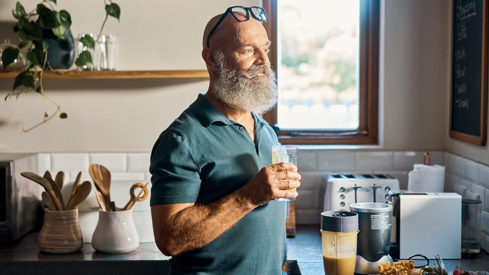 A man drinks a protein shake in his kitchen. 