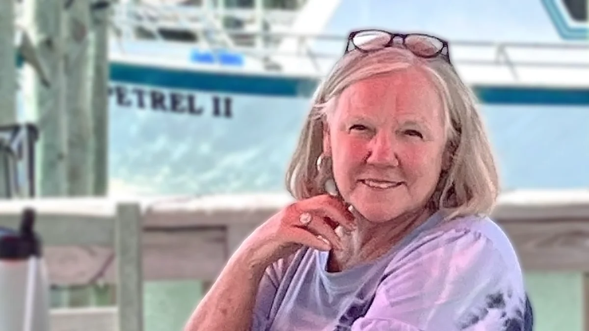 Vicki Miesbauer is pictured sitting at a restaurant by the water, with a boat behind her.