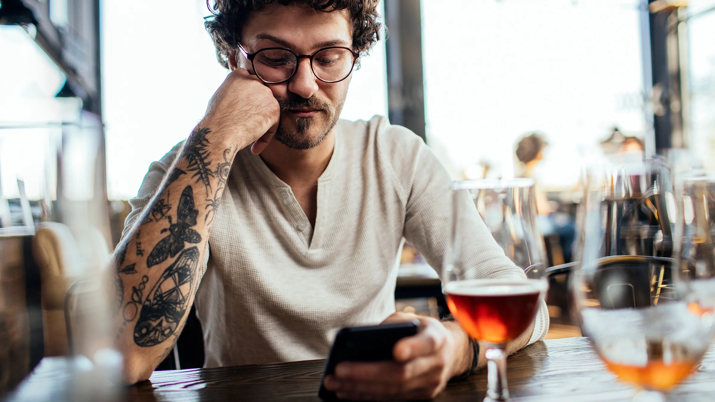 A man is looking at his phone while sitting at a bar.