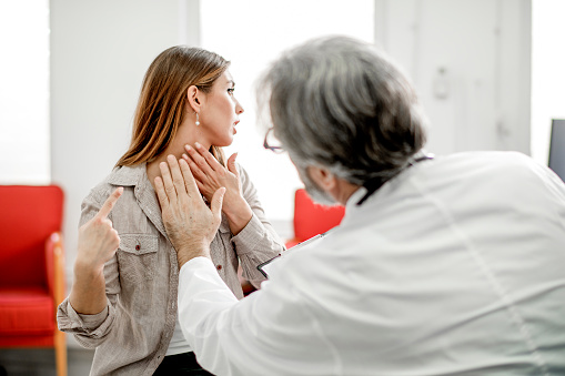Doctor checks a woman's thyroid glands by touching her neck as the woman turns her head to one side.