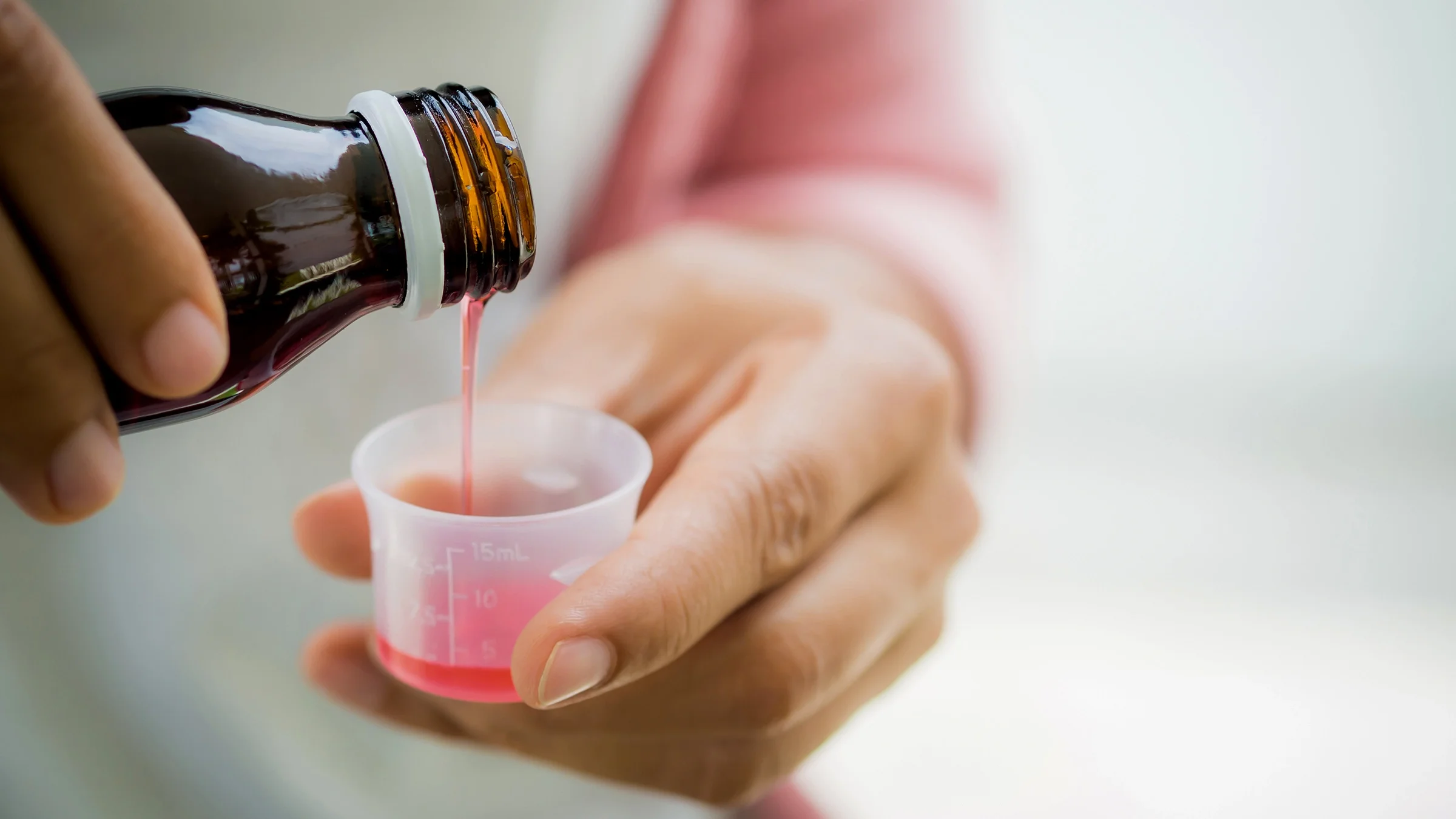 A woman pours syrup into a measuring cup.