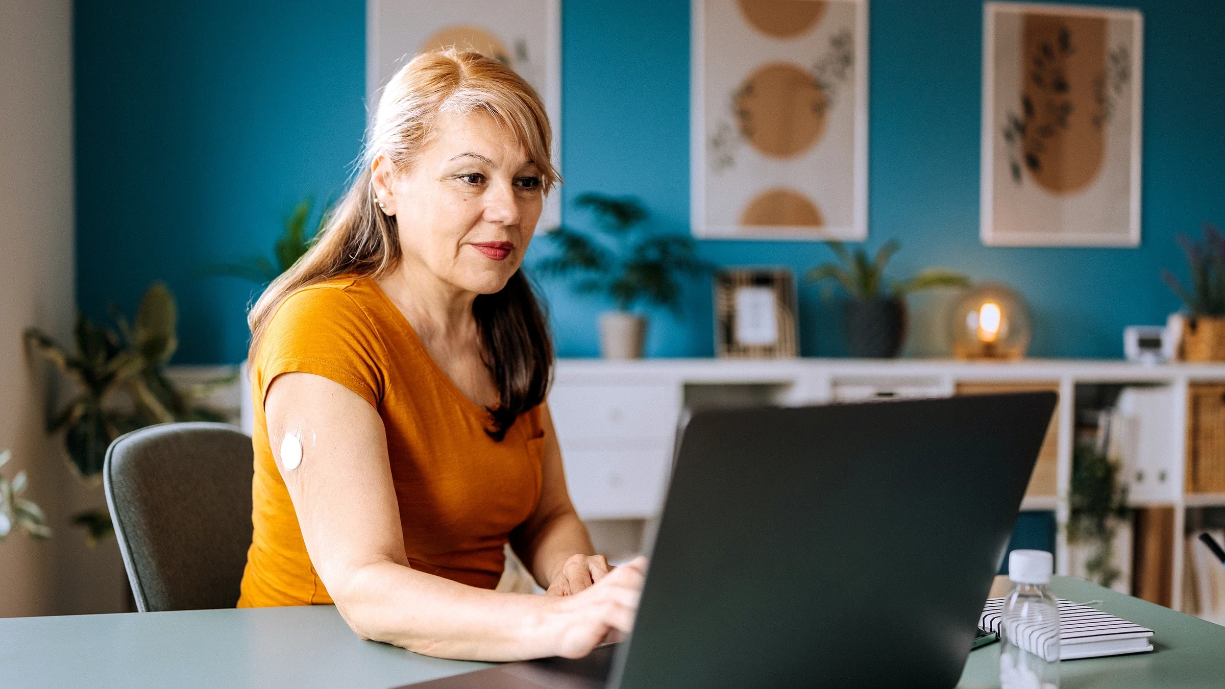 A woman with a glucose monitor on her arm uses her laptop.