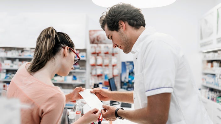 A woman reads a prescription at a pharmacy counter.