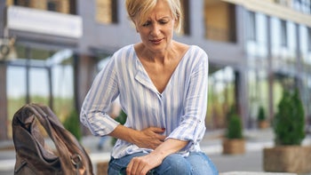 Health: Naproxen: older woman stomach pain waiting for bus-1265684688