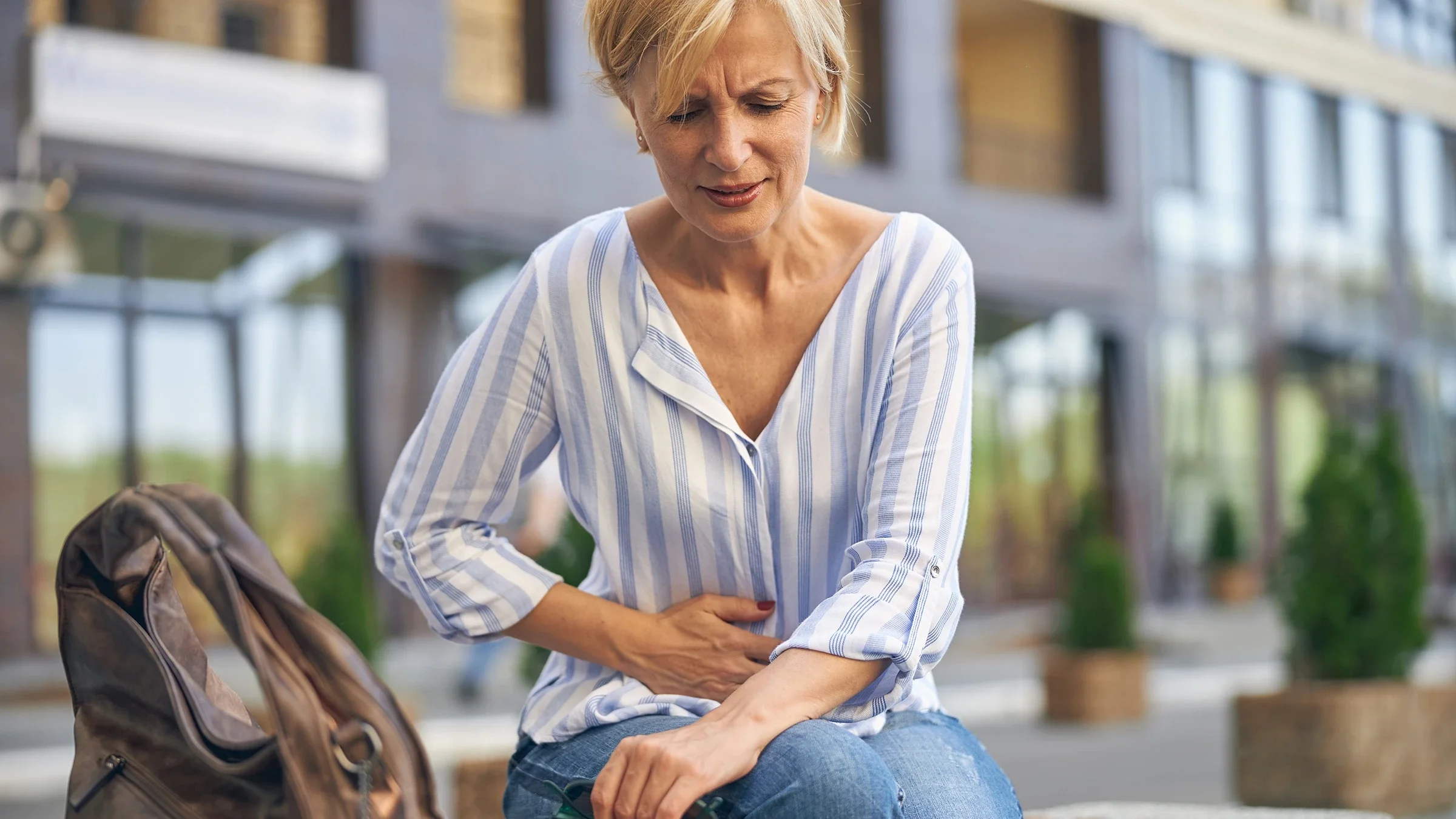 Woman sitting on a public bench grasping at her stomach in pain.