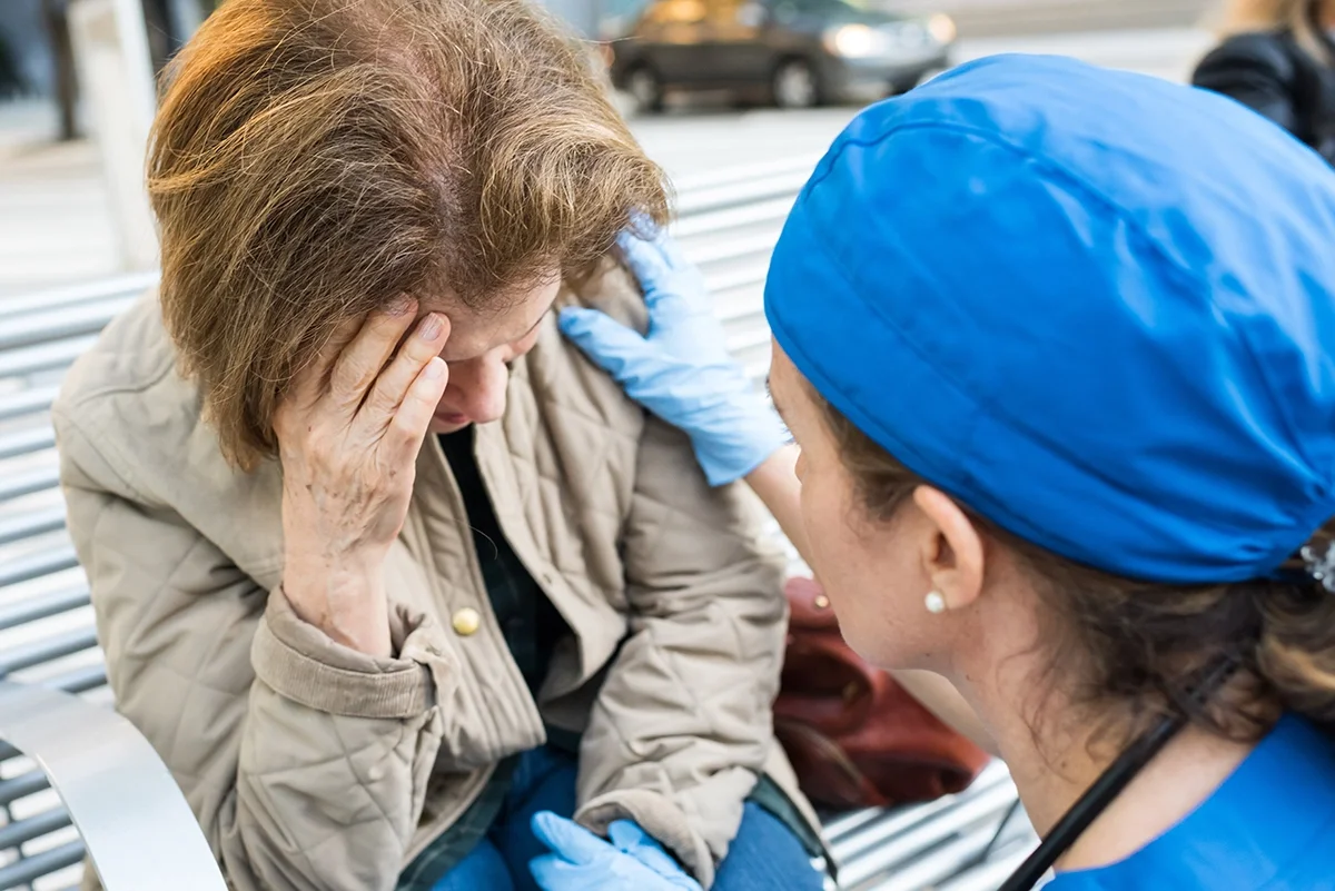 A doctor attending to a woman on a park bench experiencing confusion and other symptoms of a stroke.