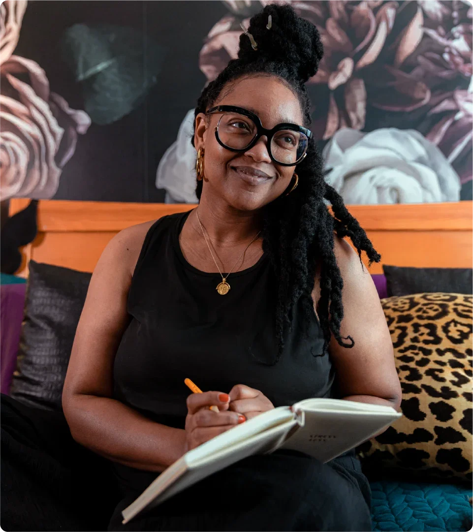 Nikki Nurse at home in bed writing in her journal. 
Original photography by BrakeThrough Media for GoodRx Health