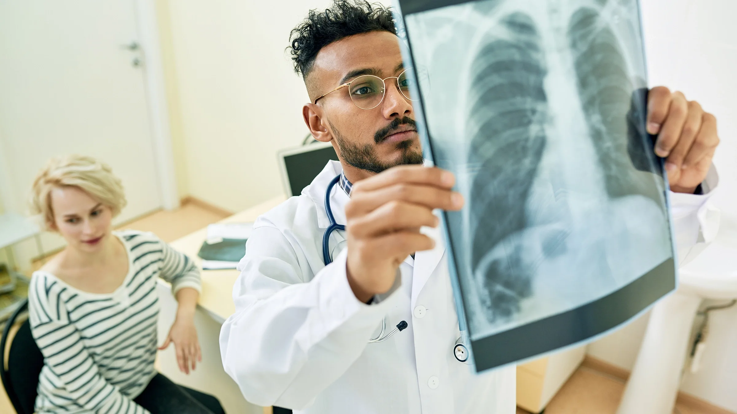 Doctor reviewing a chest X-ray with the patient in the background.