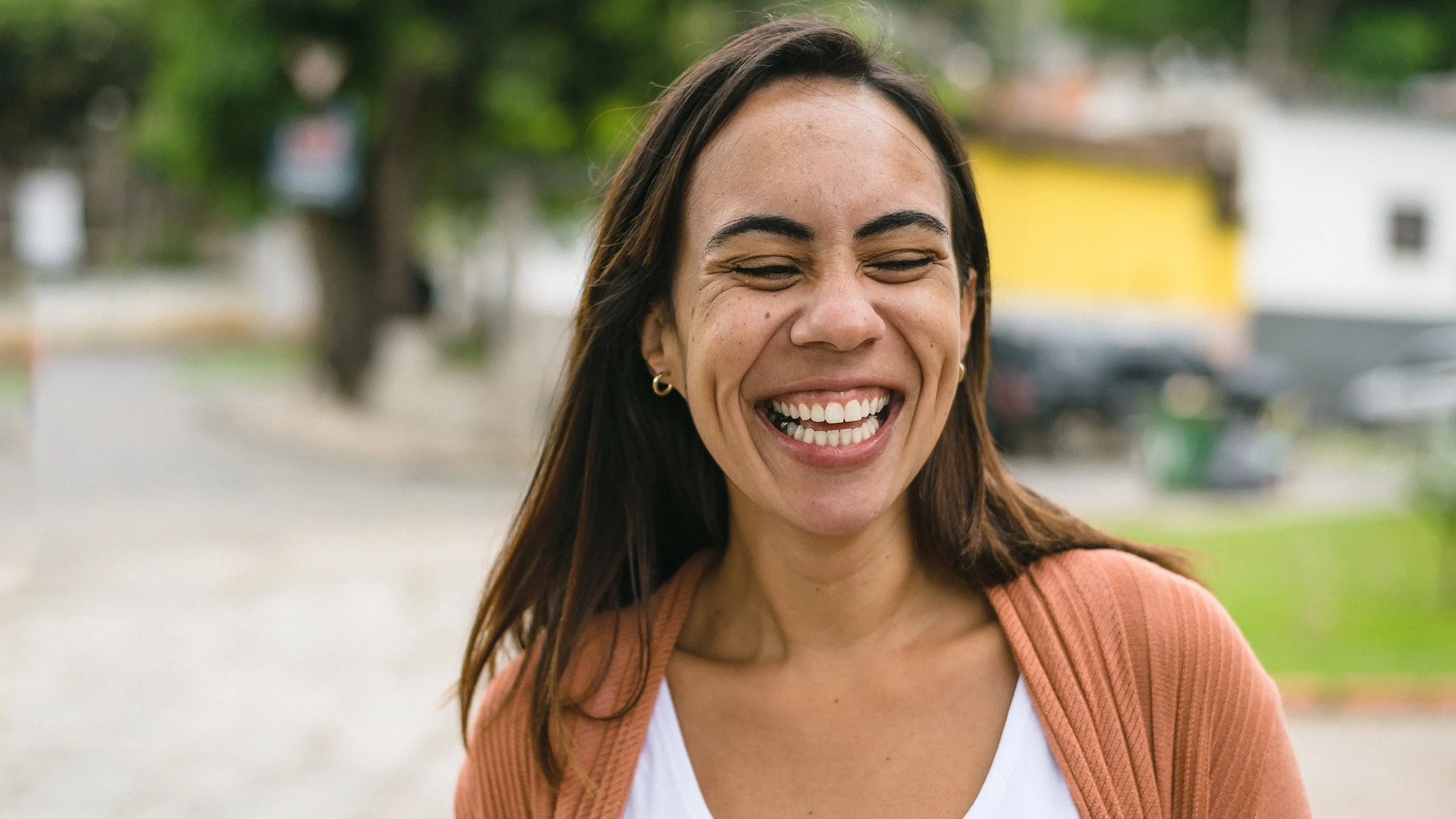 Portrait of a happy, smiling, and laughing young woman. She is outside in a park or on the sidewalk.