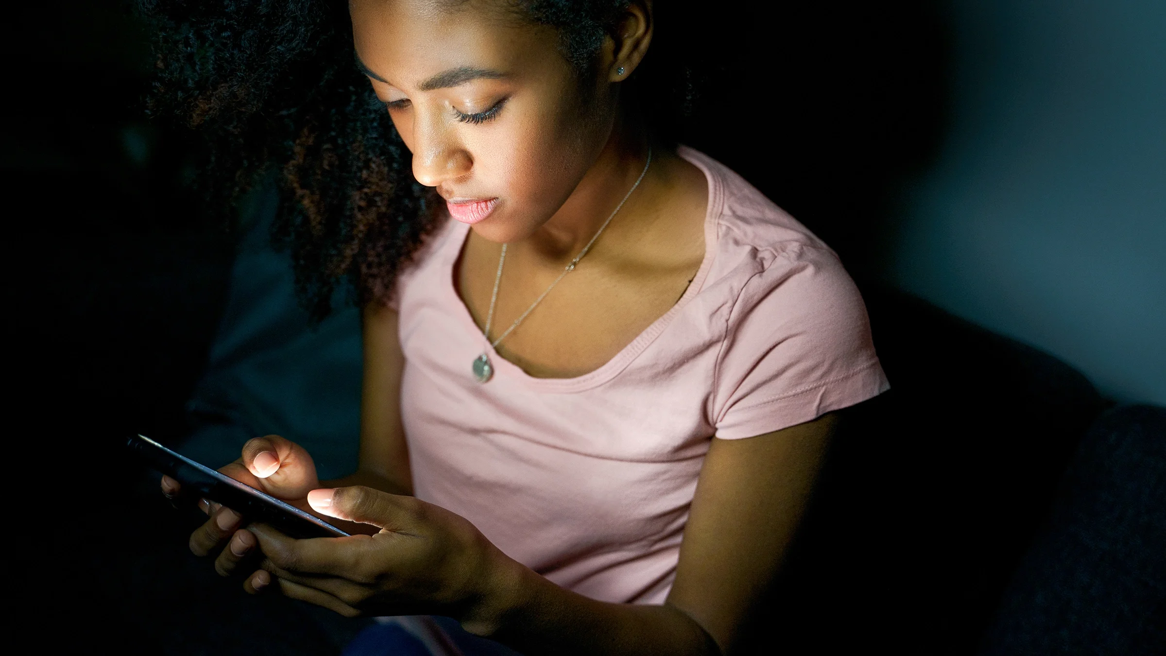 Young girl looking at her text messages on her phone in the dark.