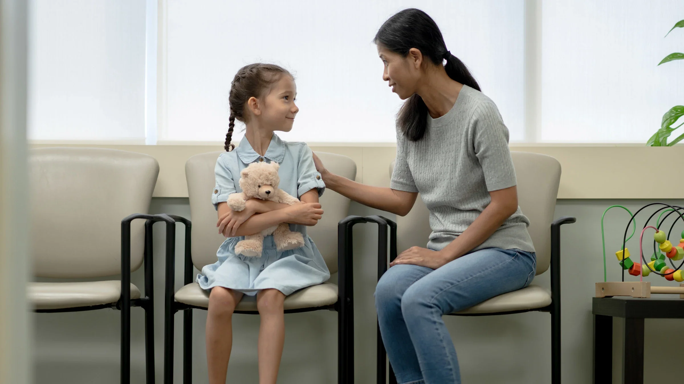 A child in a waiting room holding a teddy bear, being comforted by their parent.
FatCamera/E+ via Getty Images 