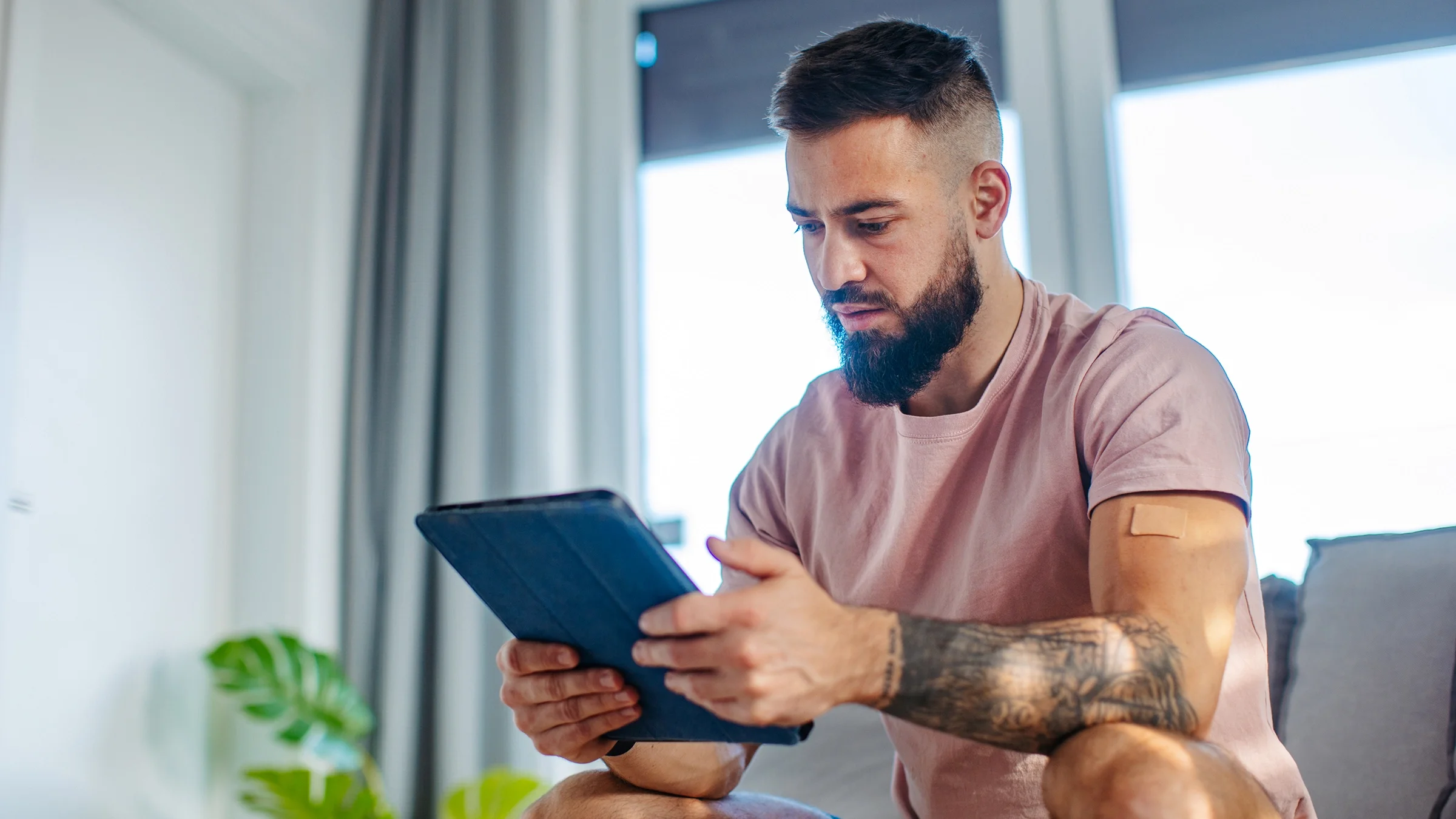 A man wearing a nicotine patch reads on a digital tablet.