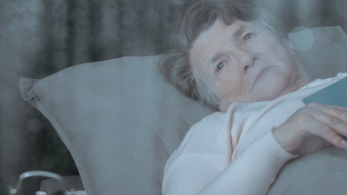 A sad senior woman  in bed looking out of her window.
