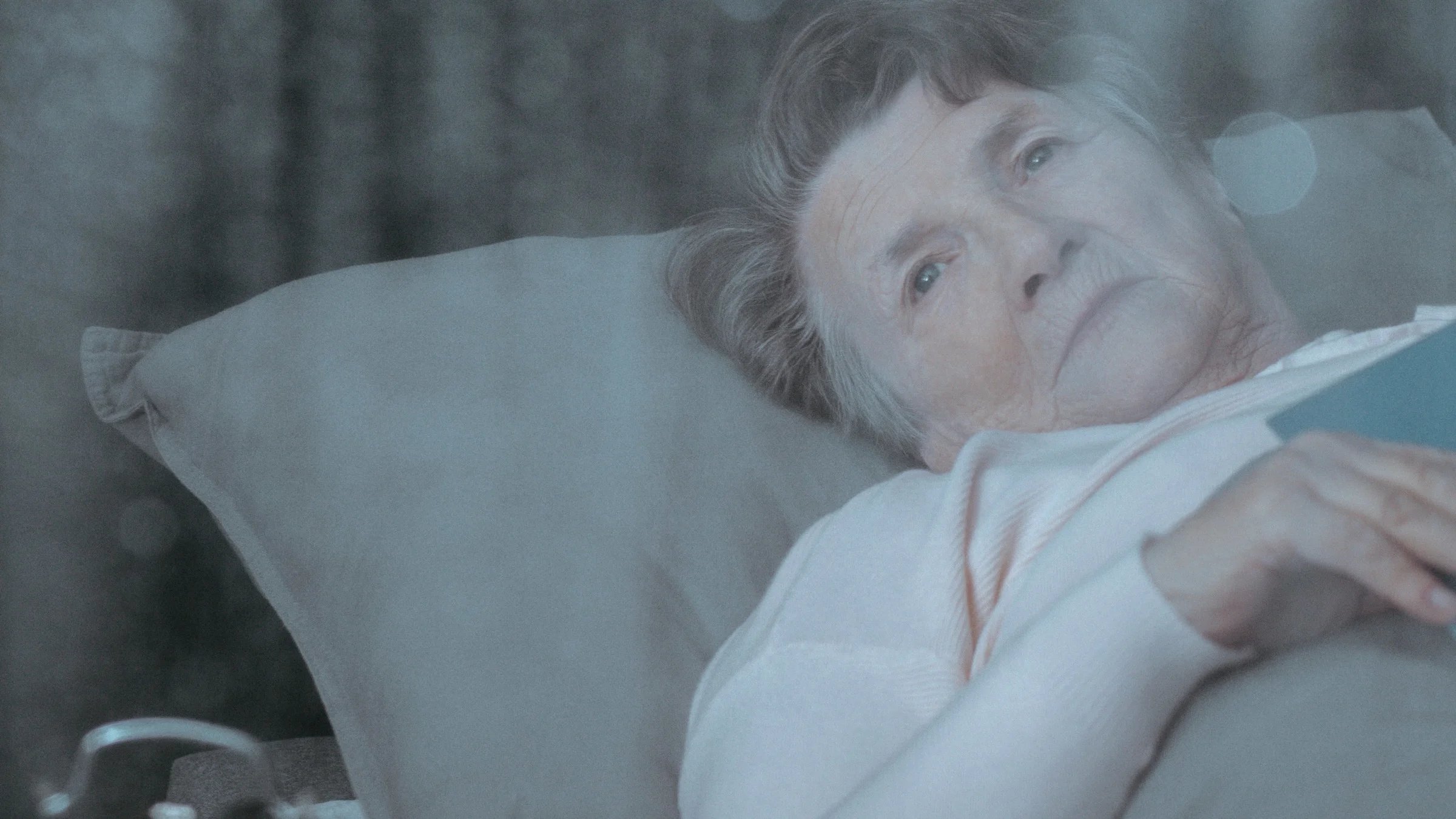 A sad senior woman in bed looking out of her window.