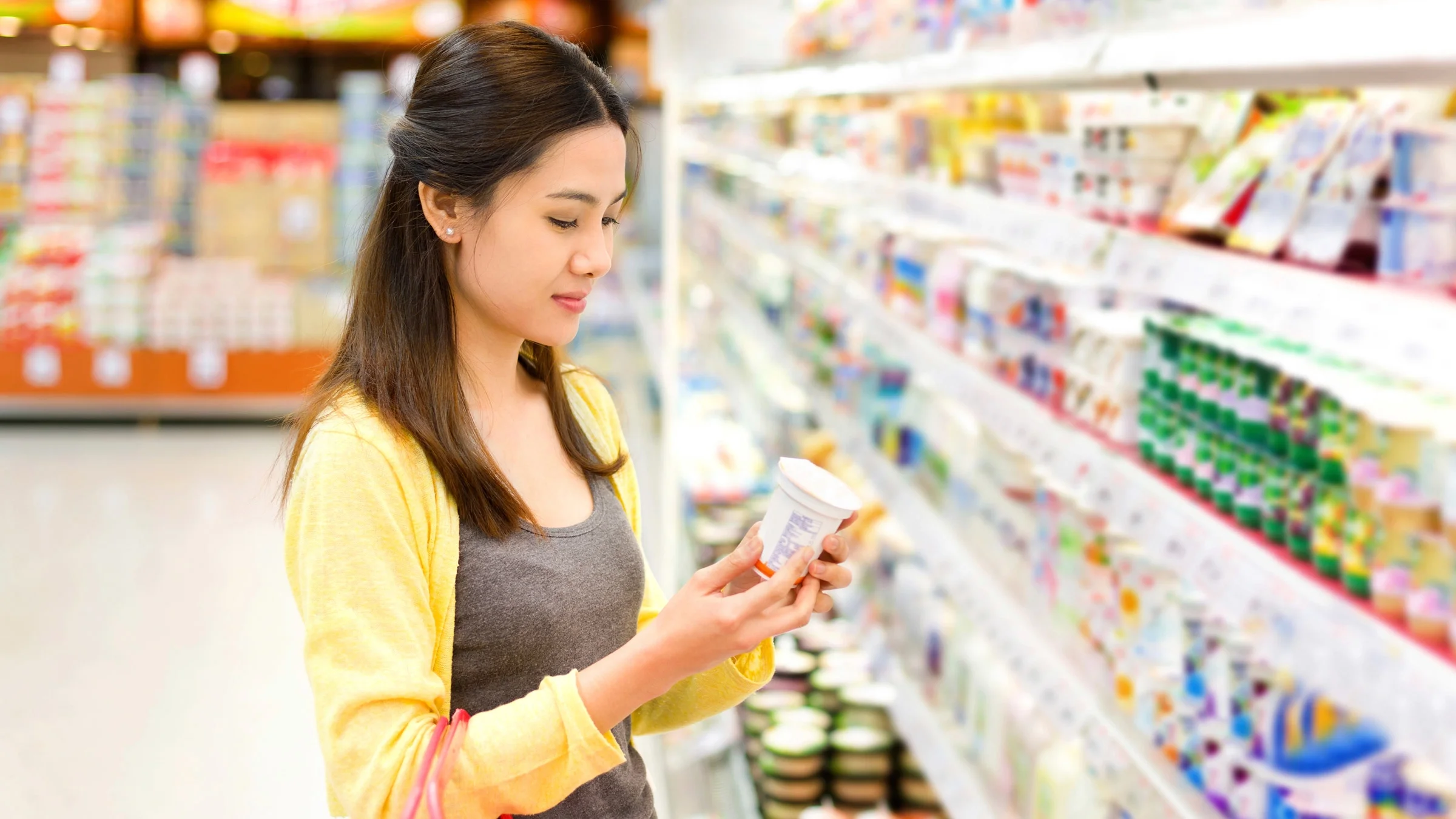 A person reading the label on a yogurt package in the grocery store.