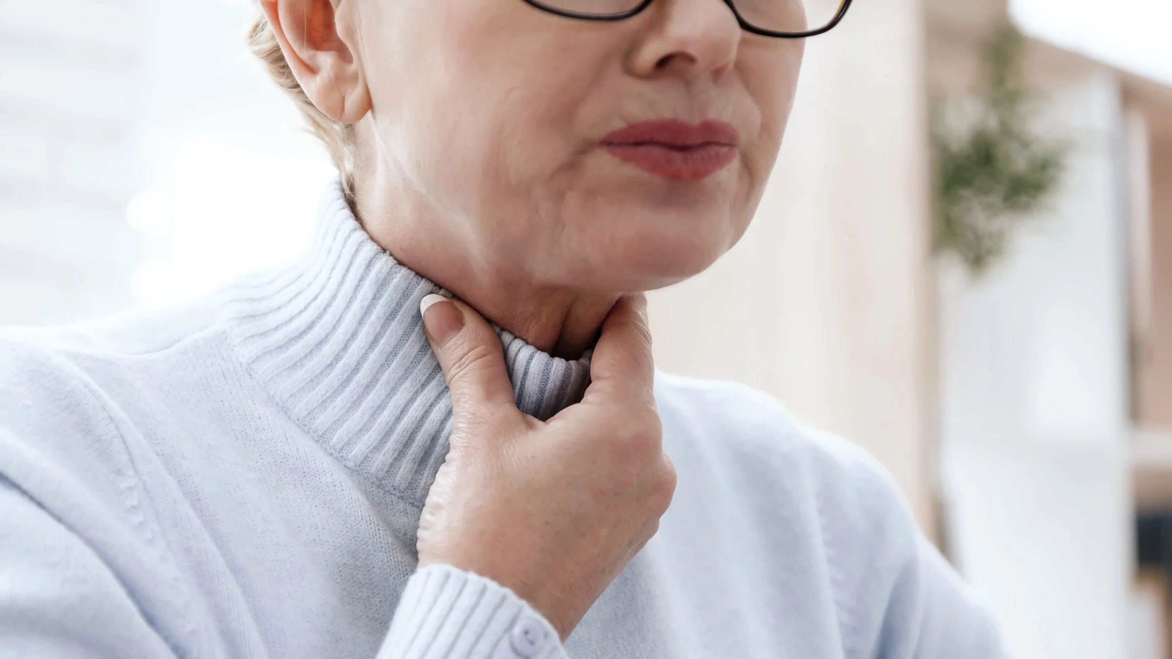 A woman holds her throat with her hands. Sore throat is one of the symptoms of eosinophilic esophagitis, which can be treated with medication and diet changes.