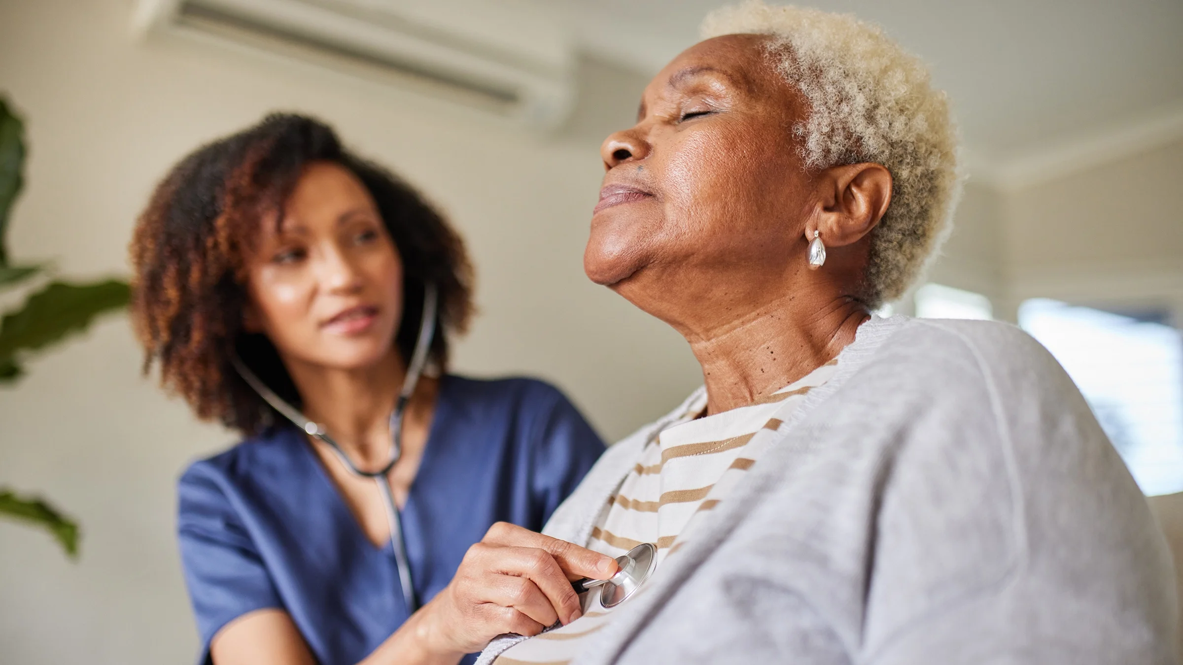 A healthcare professional listens to a woman's chest with a stethoscope.