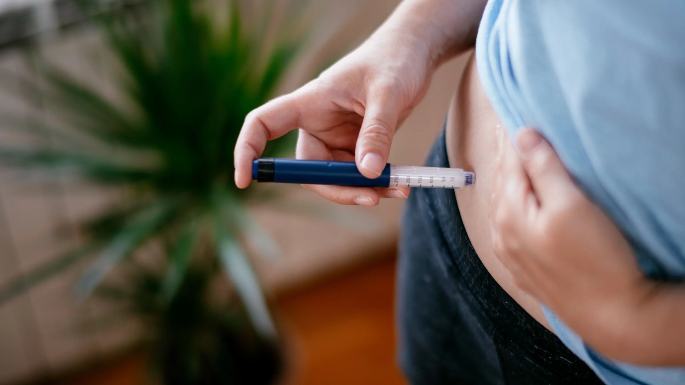 Close-up of a woman lifting her t-shirt up and using an insulin pen on her stomach.