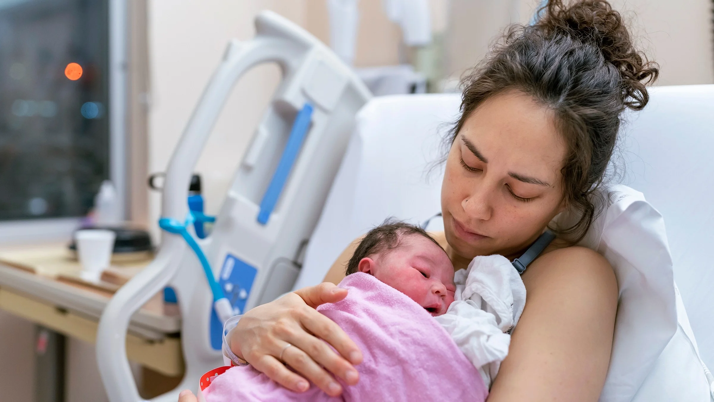 Portrait of a woman holding her newborn in the hospital bed after birth.