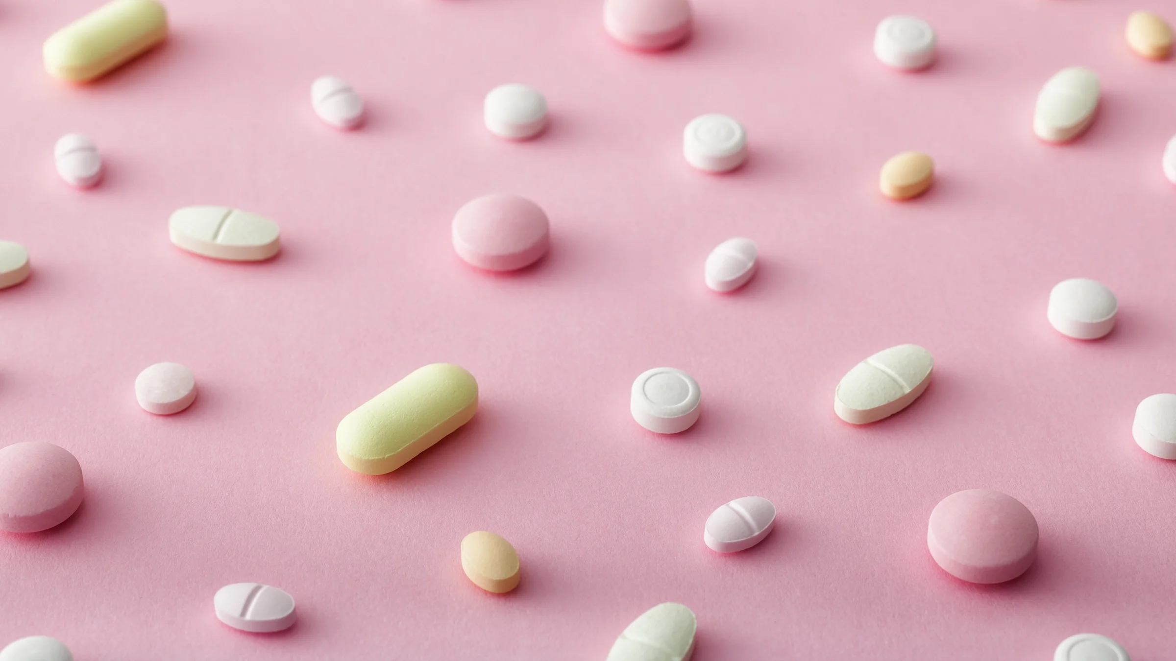 Scattered pills on a pink background.