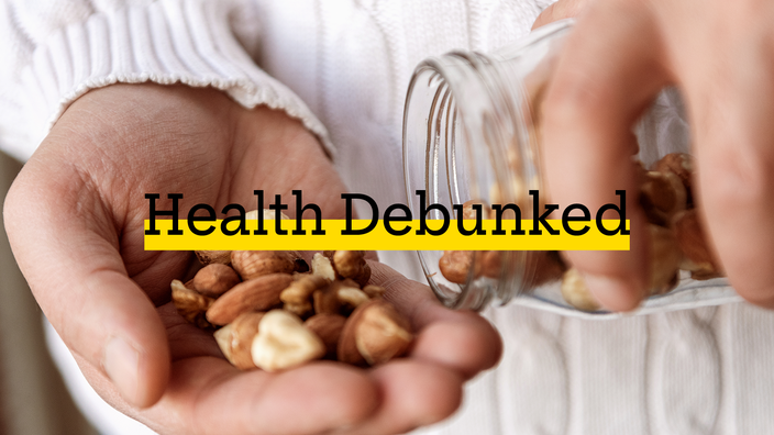 Close-up of a person pouring assorted nuts out of a mason jar into their hand. There is added text on top reading “Health Debunked” with a yellow highlight bar behind it.