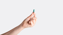 Person holding one green pill in the center of the frame. We can only see their arm reaching in holding the pill. All on a plain white studio background.
Prostock-Studio/iStock via Getty Images
