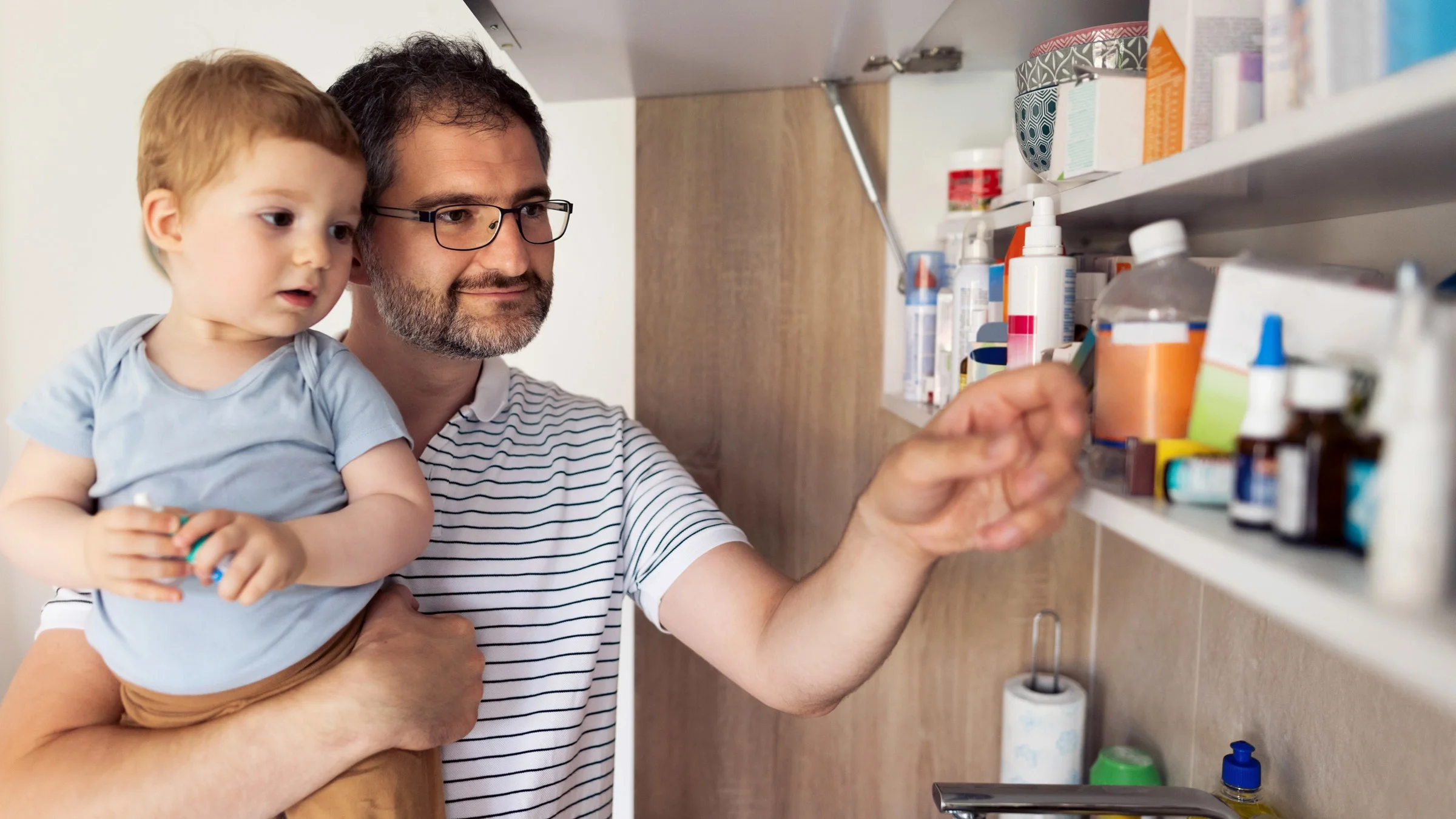 A parent holding a child and choosing medicine from their cabinet.