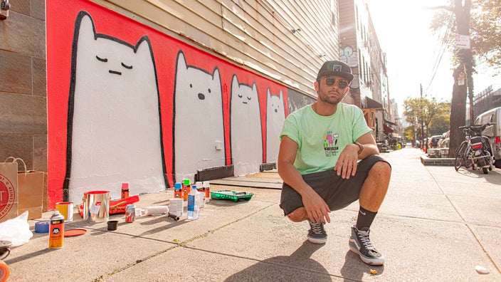 Portrait of mental health influencer Danny Casale, an animator, outside by a mural of cats.