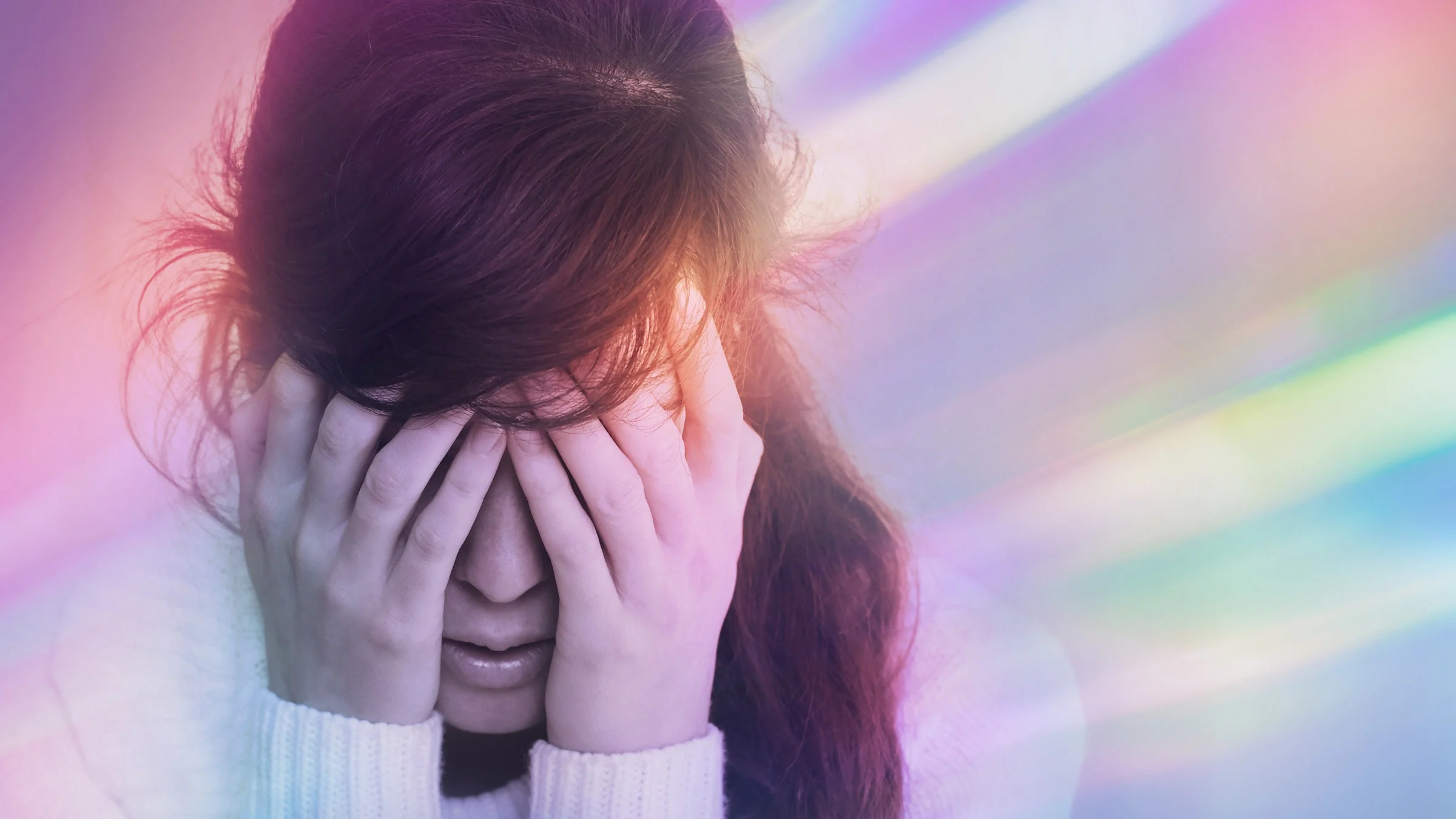 A person with a headache hiding their face, surrounded by a colorful aura.