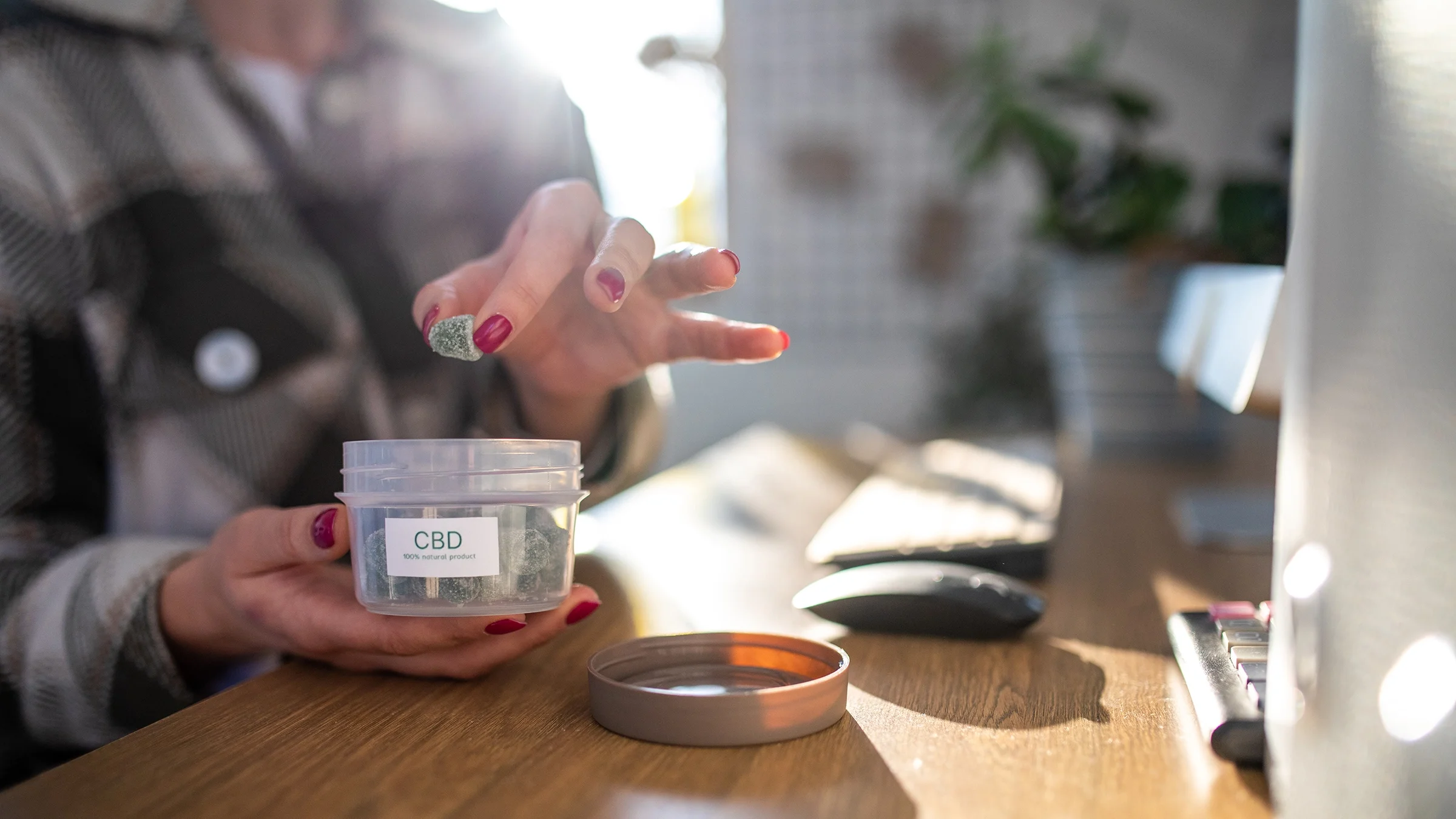 A woman picks a CBD gummy from its container.