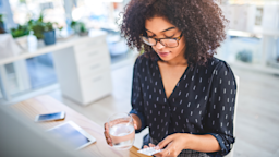 A woman is holding a glass of water and a blister pill pack.
Moyo Studio/E+ via Getty Images